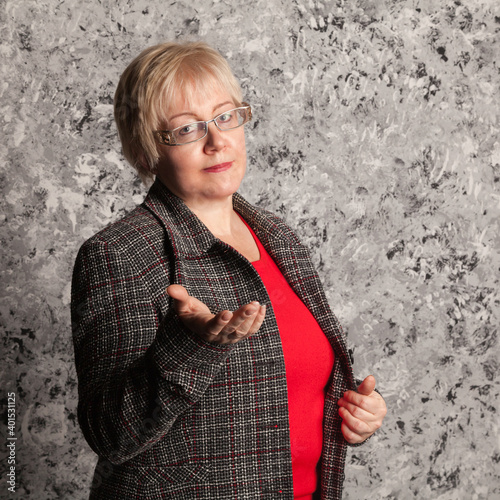 Studio portrait of blonde mature woman with short haircut in purple woolen jacket on gray textured background