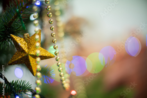 A gold star hangs on a Christmas tree as a decoration for Christmas. Shiny Christmas tree lights in the background.