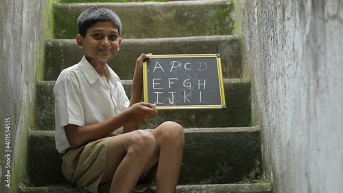 Indian child writing A B C D alphabet on Chalkboard