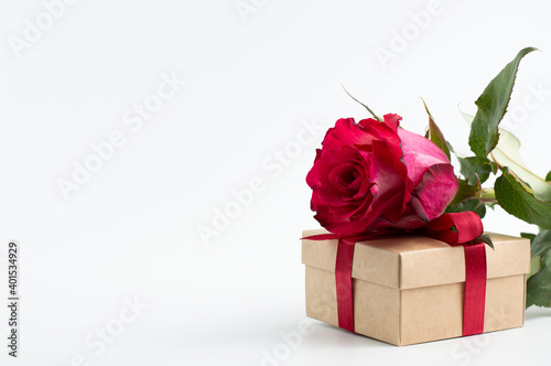 A red rose with a gift is placed on a white background with space for writing text.