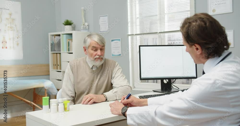 Side view of Caucasian male senior patient at doctors appointment with physician in clinic room telling symptoms. Men neurologist listening to patient about health problem. Medicine concept Side view of Caucasian male senior patient at doctors appointment with physician in clinic room telling symptoms. Men neurologist listening to patient about health problem. Medicine concept