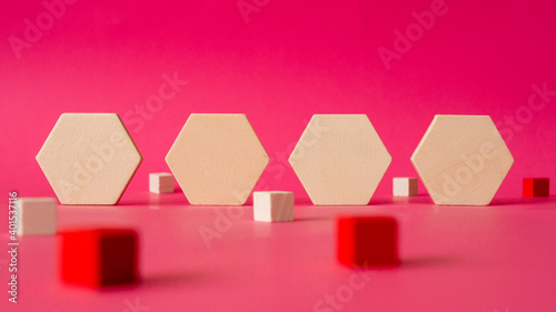 four wooden hexagonal shapes  stand against a background of pink paper with some cubes in red and white arround