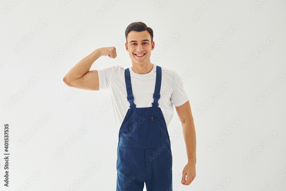 Shows biceps. Ready to work. Male worker in blue uniform standing inside of studio against white background Shows biceps. Ready to work. Male worker in blue uniform standing inside of studio against white background