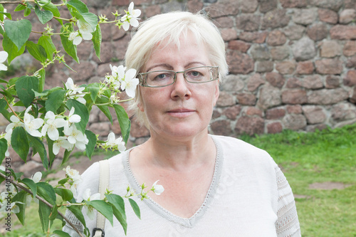 Mature blonde short haired woman in linen clothes near jasmine flowers