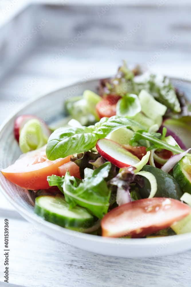 Salad with feta cheese, radish, rocket, green olives, tomatoes, cucumber and fresh basil. Bright wooden background. Close up.