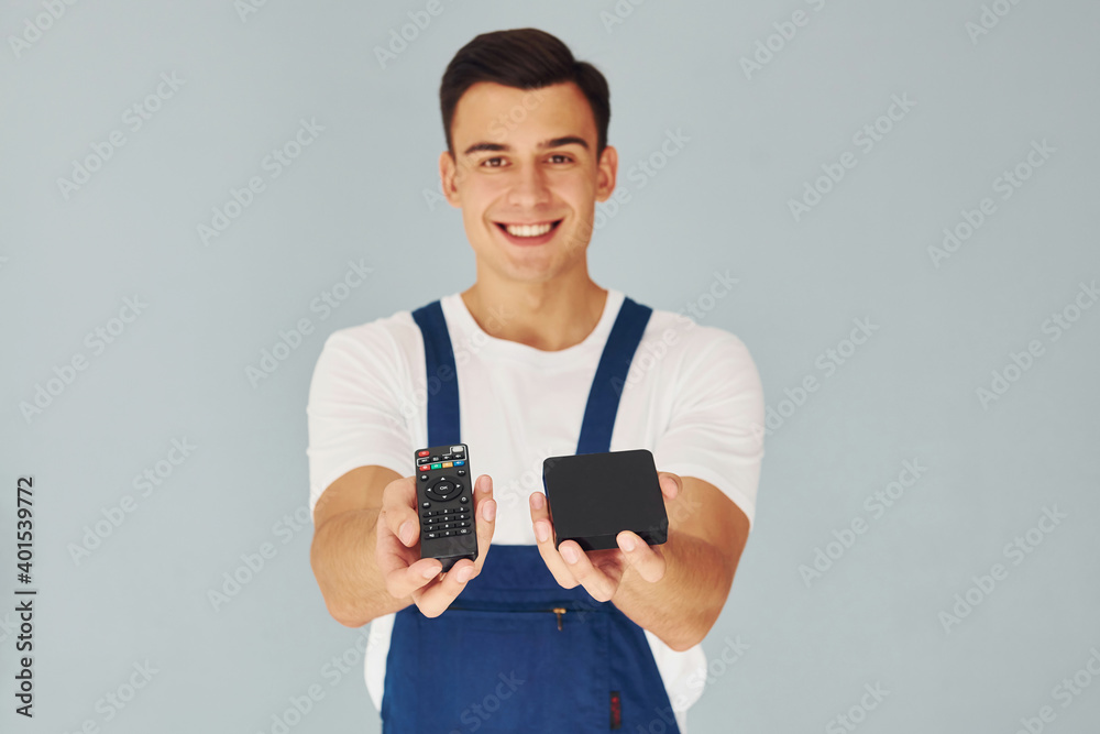 TV remote controller and smartphone. Male worker in blue uniform standing inside of studio against white background TV remote controller and smartphone. Male worker in blue uniform standing inside of studio against white background
