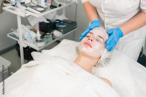 Treatment, cure of face skin in cosmetology clinic. Beauty procedure with problem skin for young woman. Cosmetologist doctor applies film on cream with anesthesia on woman's face before PRP therapy.