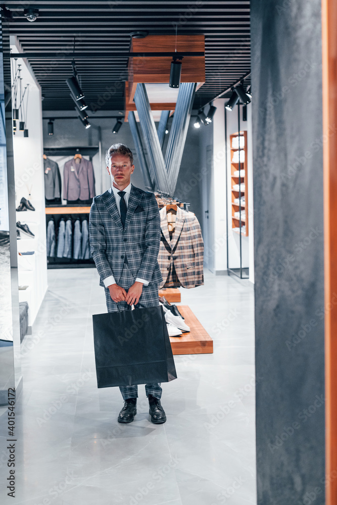 Fototapeta premium Young guy in modern store with new clothes. Elegant expensive wear for men