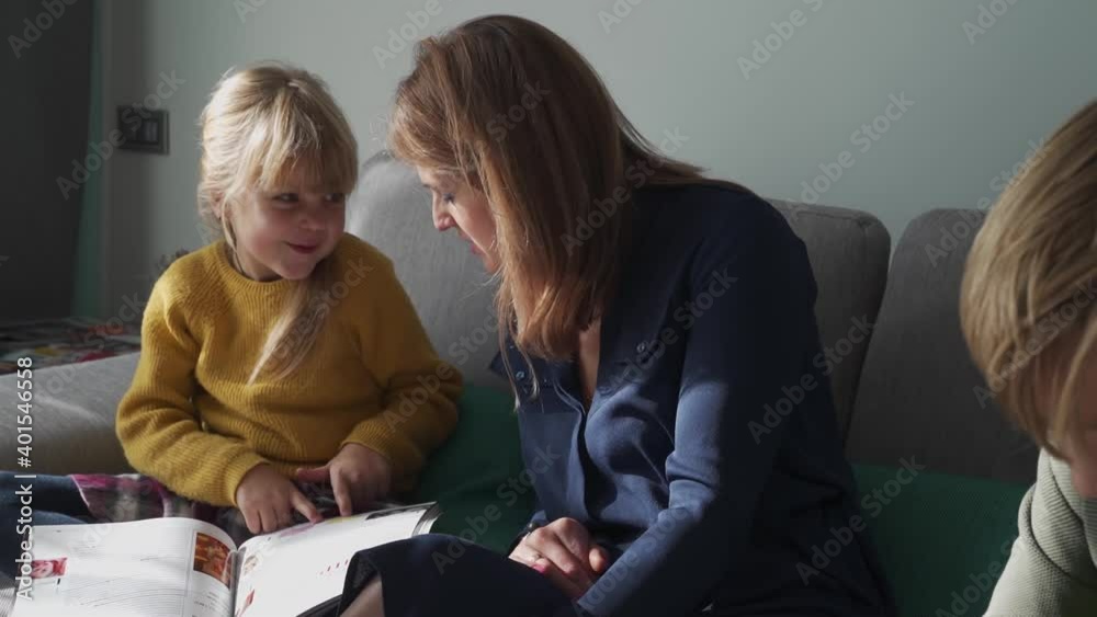 Happy family. Mom with her son and daughter are sitting on the couch at home, looking at the magazine, smiling and laughing. Family resting together. Happy family. Mom with her son and daughter are sitting on the couch at home, looking at the magazine, smiling and laughing. Family resting together.
