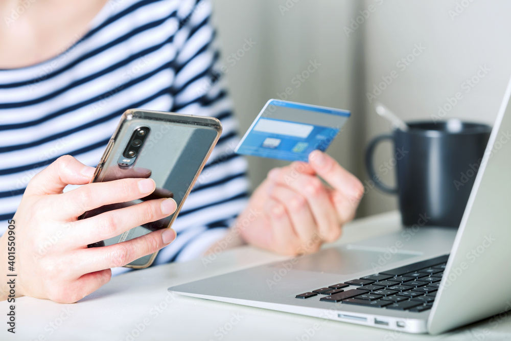  young woman with laptop using credit card and phone in kitchen at home