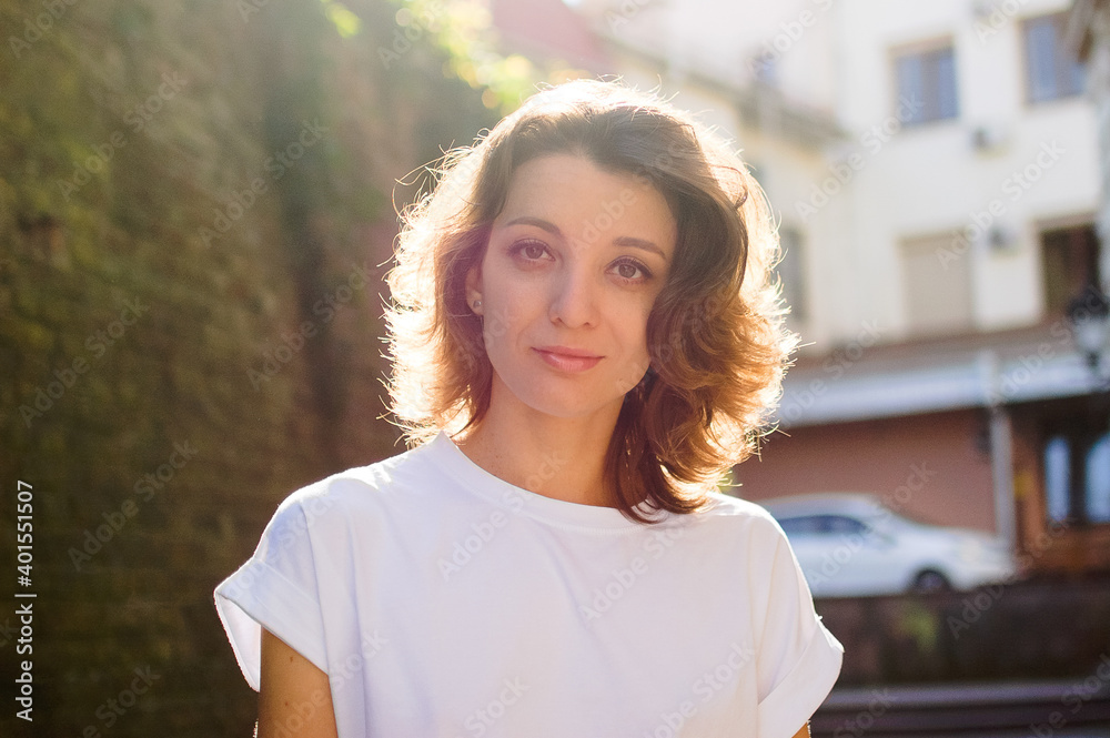 Female portrait of beautiful student, pretty girl with short hair in white t-shirt spending time outdoors near old stone wall during sunny spring or summer day Female portrait of beautiful student, pretty girl with short hair in white t-shirt spending time outdoors near old stone wall during sunny spring or summer day