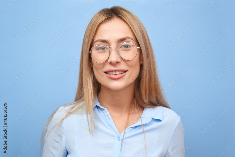 portrait beautiful young blond woman in business shirt with glasses toothy smiling and looking at the camera isolated on blue studio background with copy space portrait beautiful young blond woman in business shirt with glasses toothy smiling and looking at the camera isolated on blue studio background with copy space