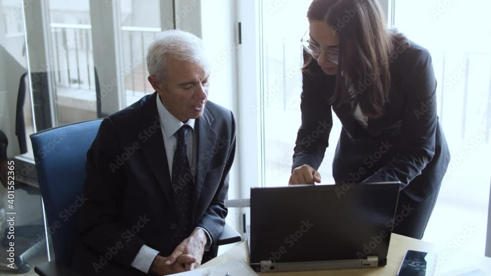 Female project manager explaining report details to male boss, pointing at document and speaking. Medium shot. Business and cooperation concept