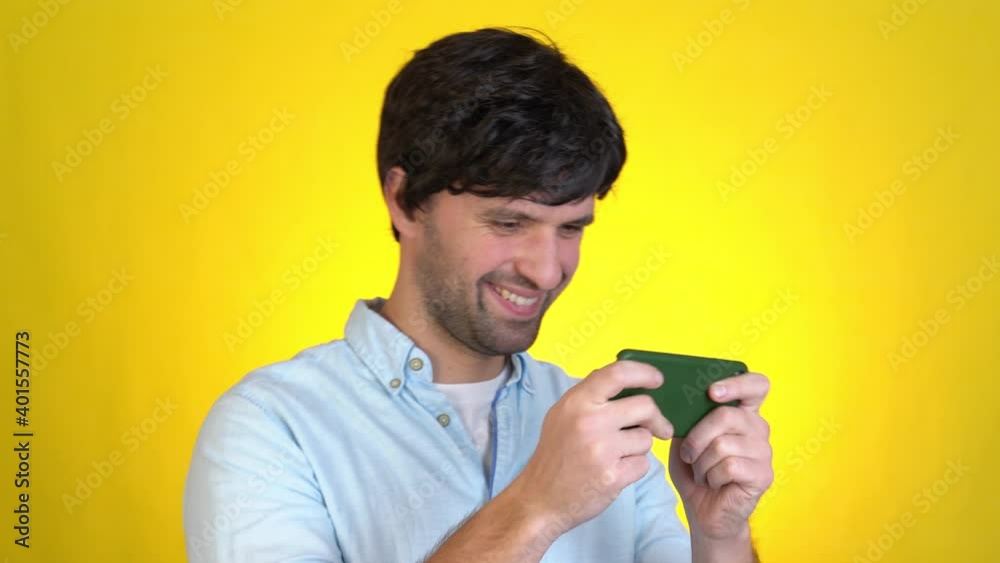 Gambling young man play mobile cell phone hold gadget smartphone video pc games isolated on yellow background studio People lifestyle concept Gambling young man play mobile cell phone hold gadget smartphone video pc games isolated on yellow background studio People lifestyle concept