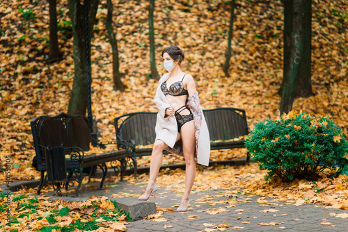 Fashion portrait of sexy woman in face mask and bodysuit in autumn park. Pandemic, coronavirus