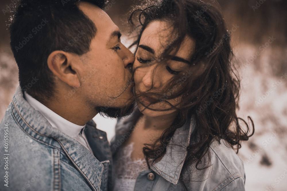 Hispanic man in denim jacket oversized and woman in love are kissing hugging in winter in snow Hispanic man in denim jacket oversized and woman in love are kissing hugging in winter in snow