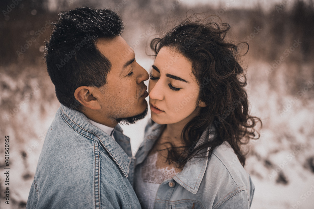 Hispanic man in denim jacket oversized and woman in love are kissing hugging in winter in snow Hispanic man in denim jacket oversized and woman in love are kissing hugging in winter in snow