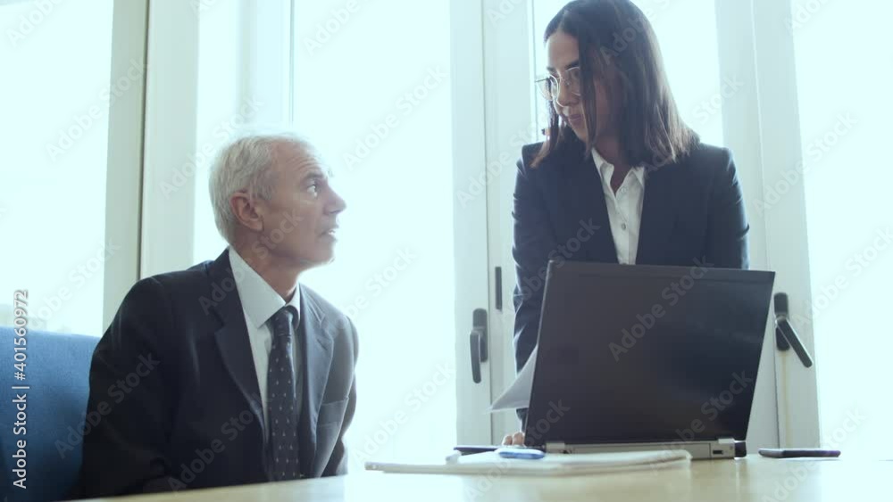 Serious female assistant explaining paper details to male boss, pointing at document and speaking. Medium shot. Business and cooperation concept Serious female assistant explaining paper details to male boss, pointing at document and speaking. Medium shot. Business and cooperation concept