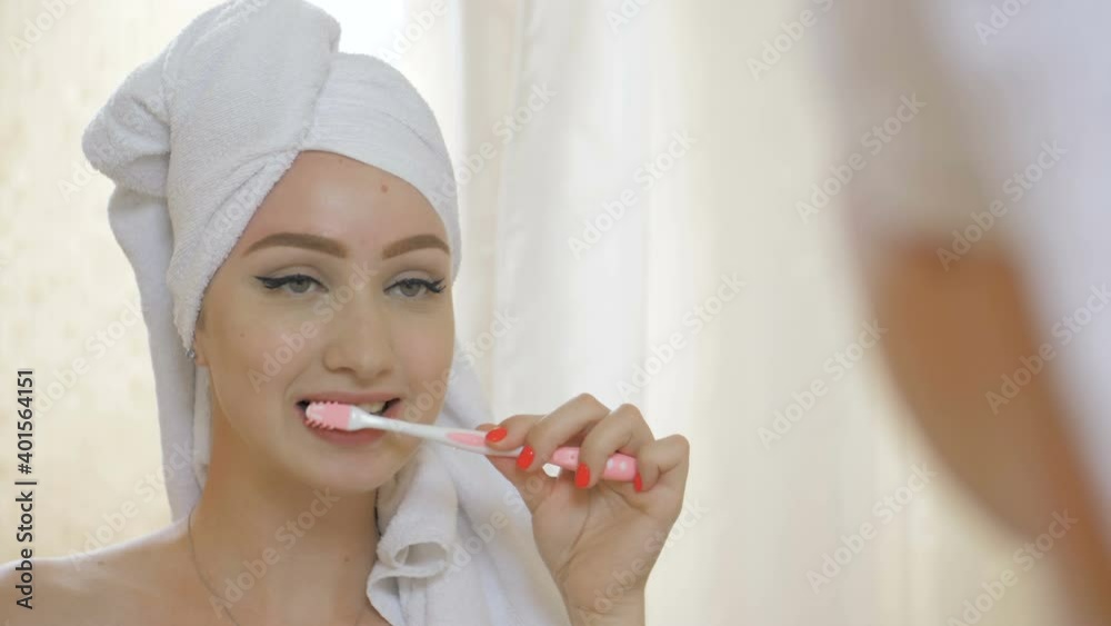 Young pretty girl in towel brushing teeth in front of the mirror in bathroom Young pretty girl in towel brushing teeth in front of the mirror in bathroom