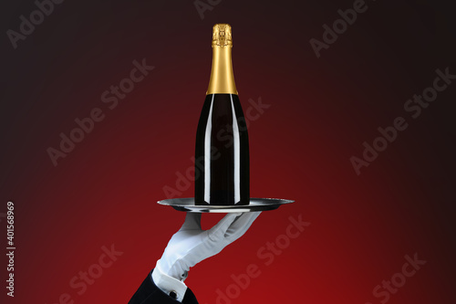 Closeup of a waiters hand and silver tray with Champagne Bottle, over red spot background. © Steve Cukrov