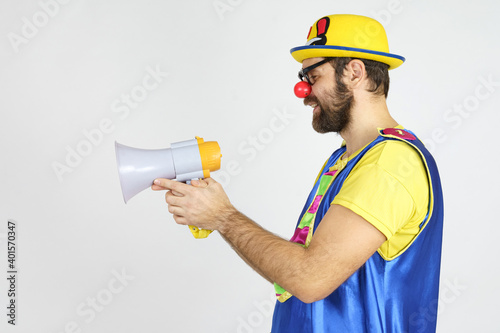A clown in a bright blue and yellow suit, glasses and a hat plays with a megaphone.