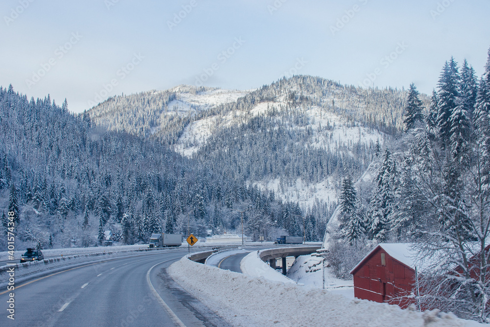 Snow-covered highway among the mountains, on the sides there are trees and trees in the snow. Winter landscape with snow-covered road, fir trees and mountains in Montana, America, 1-18-2020