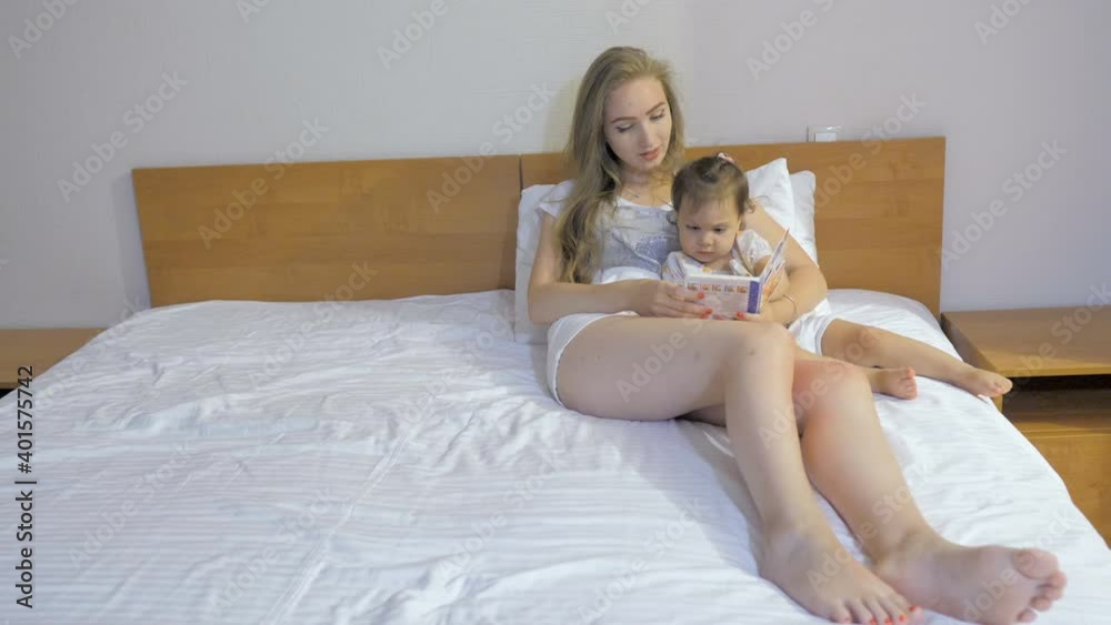 Young mother reading a book to her daughter in a bedroom Young mother reading a book to her daughter in a bedroom