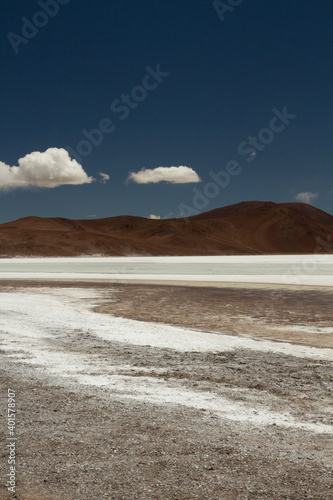 The white desert. Natural salt flats in the cordillera. View of the white salt field and brown mountains under a deep blue sky.