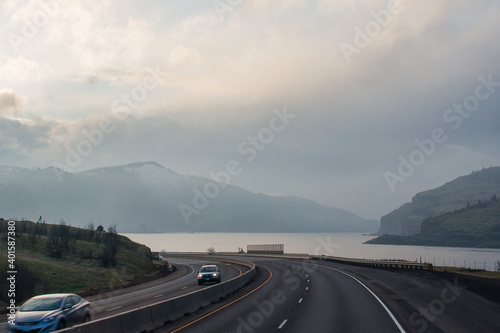 A highway among the mountains, on one side of the road there is a large river, in winter or late autumn, along which cars travel