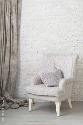 soft armchair near white brick wall with gray curtain. Arm-chair with gray upholstery © Olga Mishyna