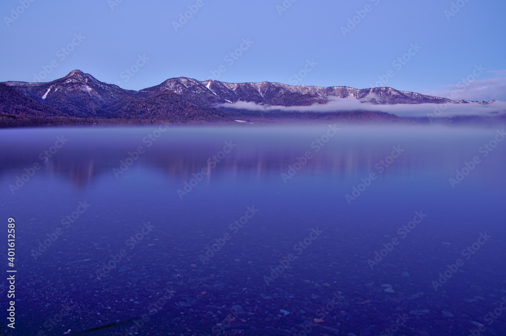 冬山と静水の湖面。夜明けの湖の風景。