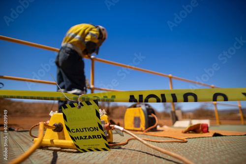 Safety workplace yellow striped caution tape sign barricade exclusion zone preventing from public access while construction worker welder welding repairing fence 