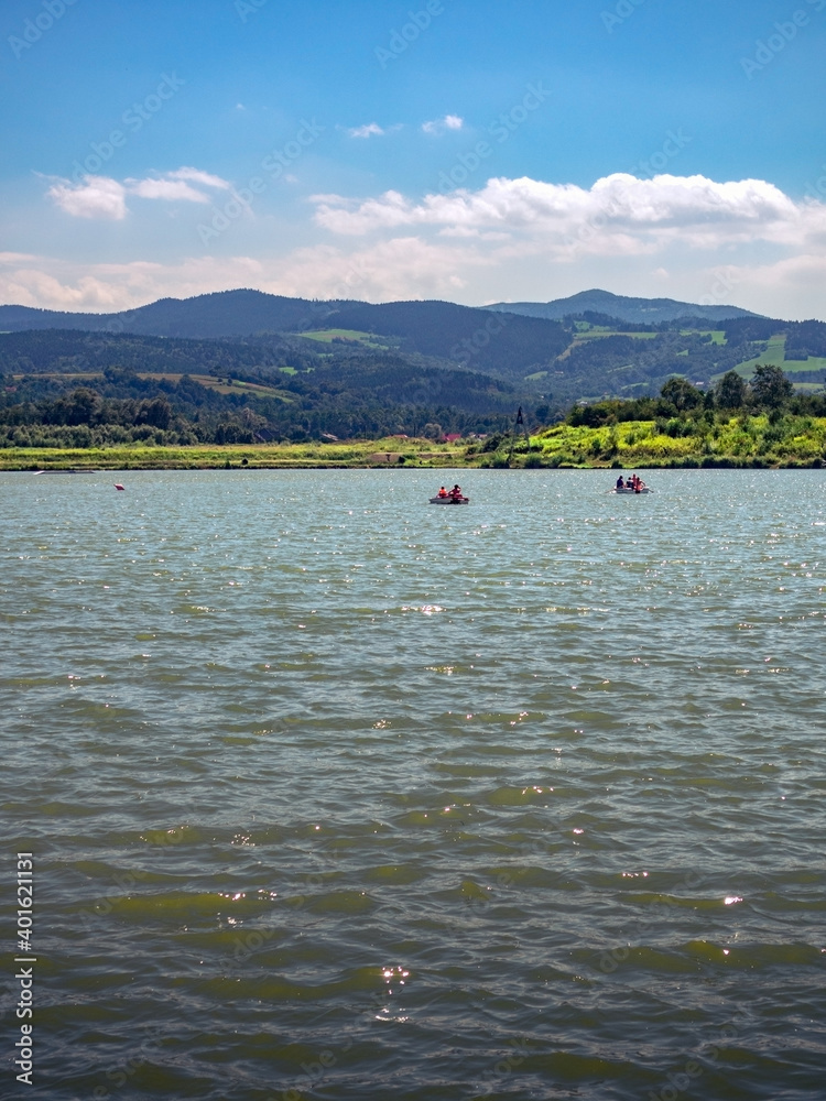 People boating on lake at mountains background. Stary Sacz, Poland.