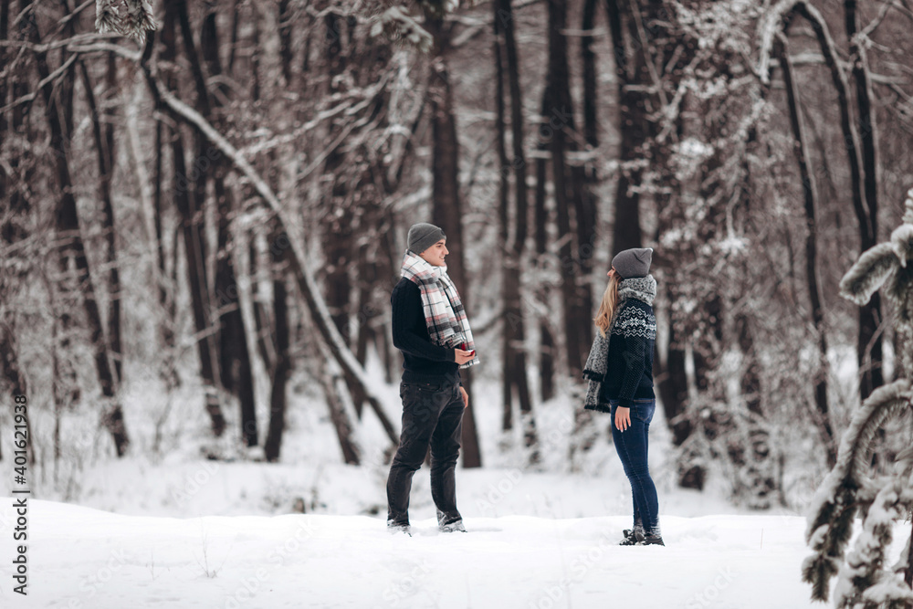 Kneeling guy puts an engagement ring on a girl's hand, making a proposal to get married in winter in a snowy forest