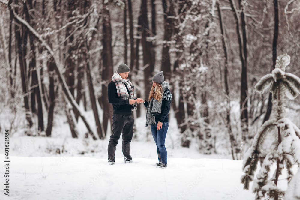 Kneeling guy puts an engagement ring on a girl's hand, making a proposal to get married in winter in a snowy forest