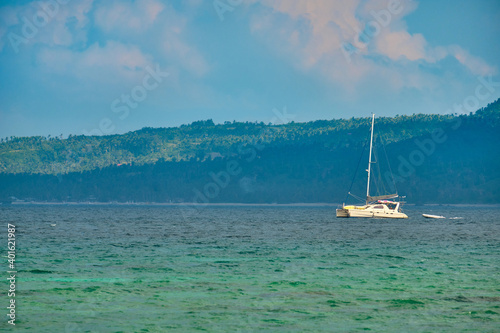Philippines, Boracay island, Puka Beach. A white yacht is moored in the sea with a white rubber boat attached. Against the background of the mountain and palm trees of the neighboring island.