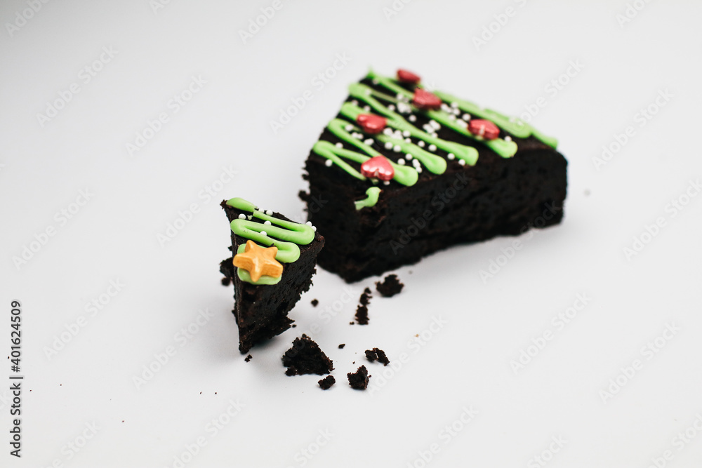 Slice of Fresh Homemade Chocolate Brownie with green icing and festive sprinkles close up. Sweet homemade Christmas or winter holidays pastry food concept.