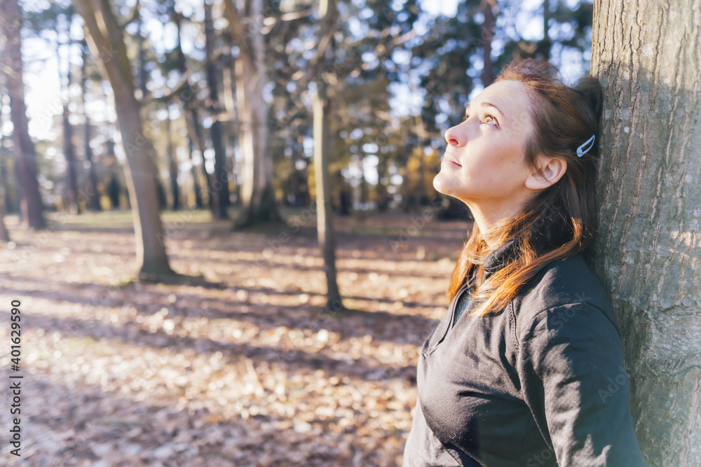 beautiful woman leaning on tree trunk in the forest thinking and enjoying the good weather. beautiful woman leaning on tree trunk in the forest thinking and enjoying the good weather.