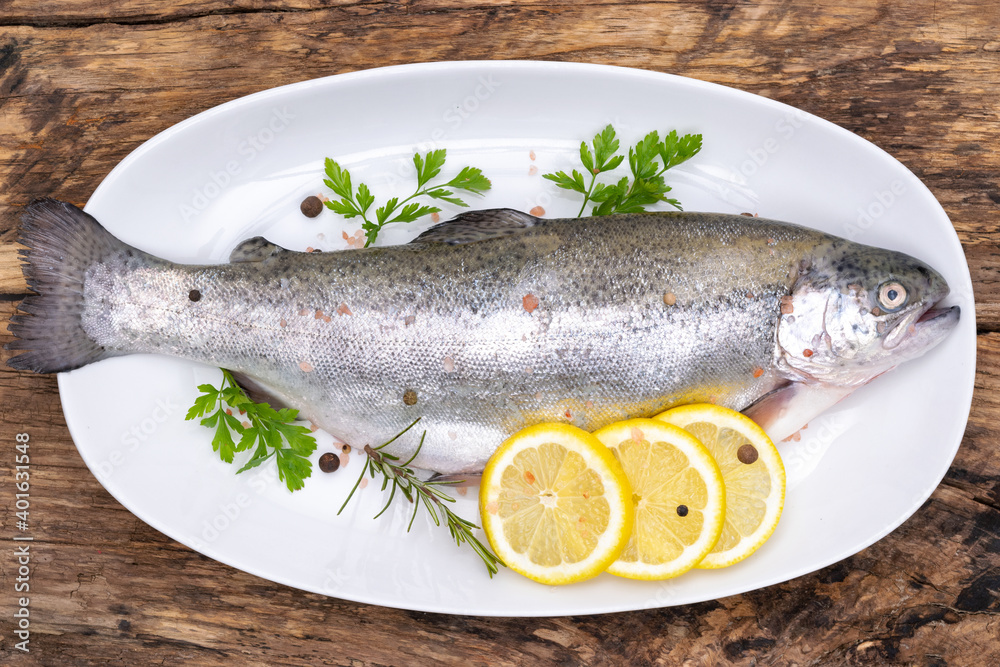 Top view of a raw rainbow trout marinated in fresh herbs and lemon ready for cooking on a plate in rustic style Top view of a raw rainbow trout marinated in fresh herbs and lemon ready for cooking on a plate in rustic style