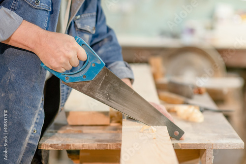Carpenter sawing a board with a hand wood saw in carpentry workshop