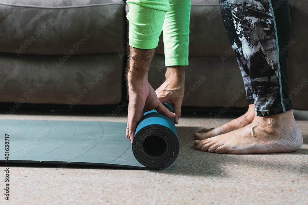 Middle-aged man picks up a yoga mat at home
New normal concept, exercising at home