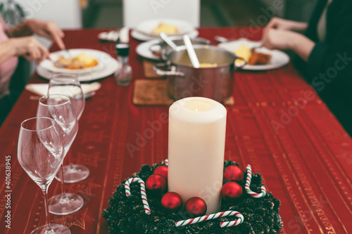 Foreground focus on empty wine glasses and candle  with two women having lunch on Christmas table in background