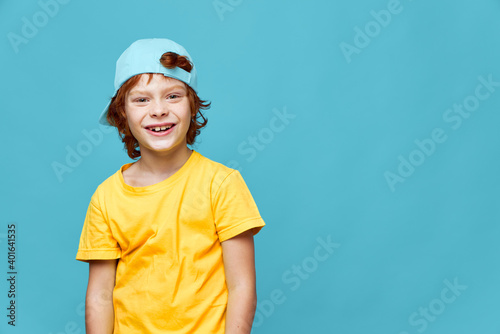 Cheerful boy red hair blue cap on his head yellow t-shirt Copy Space