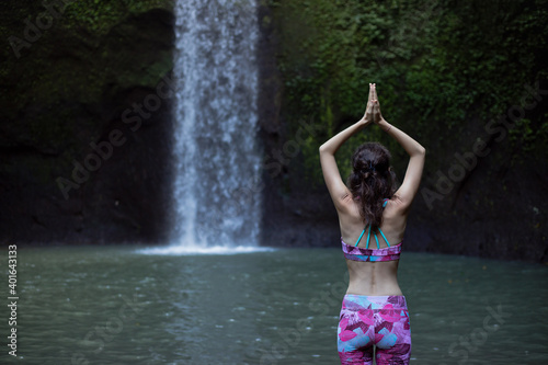 Hands raising up in namaste mudra. Woman meditating  practicing yoga and pranayama with namaste mudra near waterfall. Yoga outdoor concept. Tibumana waterfall  Bali. Copy space. View from back.