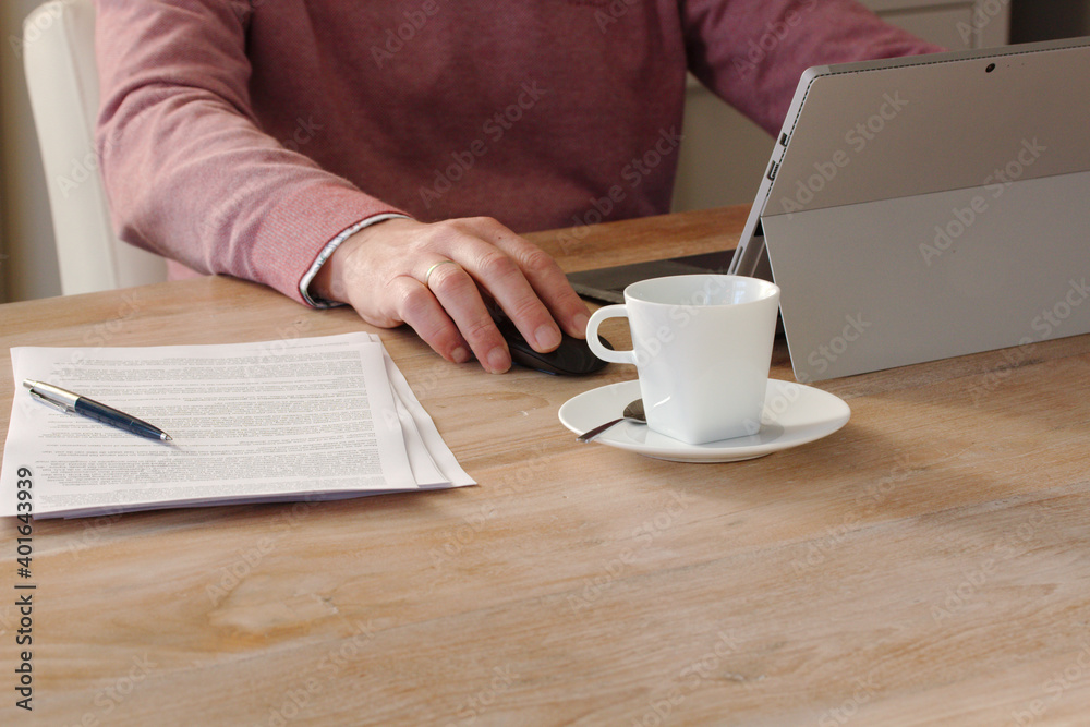 person working at home on a laptop with a cup of coffee, pen and stack of paper on a wooden table background person working at home on a laptop with a cup of coffee, pen and stack of paper on a wooden table background