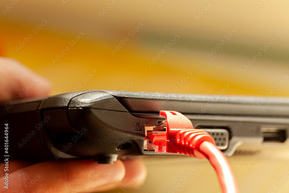 Laptop red network cable connected, netbook internet connection port closeup, detail, copy space. Thin notebook with rj45 plug, side view. Web access, broadband service provider, going online concept Laptop red network cable connected, netbook internet connection port closeup, detail, copy space. Thin notebook with rj45 plug, side view. Web access, broadband service provider, going online concept