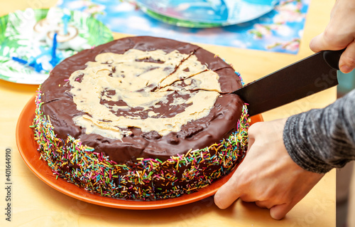 Fotografija Person cutting, dividing a homemade chocolate cake decorated with many sprinkles using a knife, hand closeup