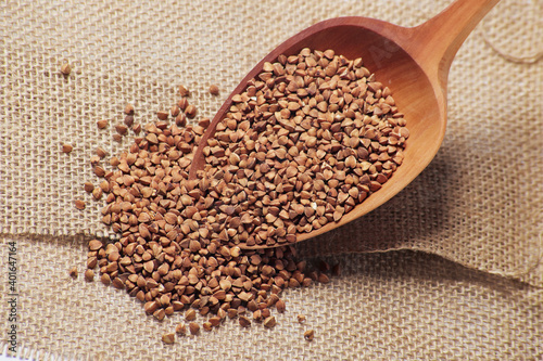 Top view of uncooked buckwheat grain seeds in the wooden spoon on the background of sackcloth