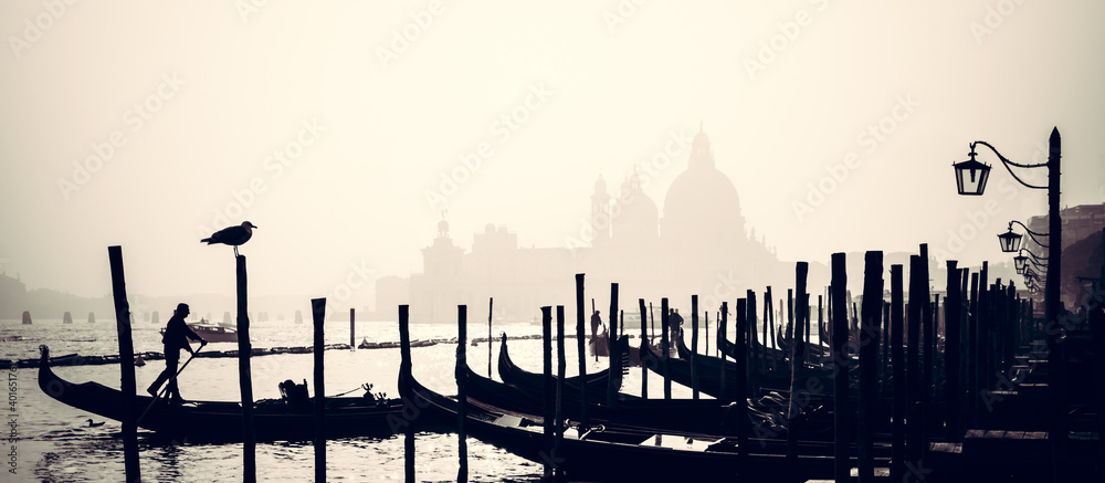 Romantic Italian city of Venice, a World Heritage Site: traditional Venetian wooden boats, gondolier and Roman Catholic church Basilica di Santa Maria della Salute in the misty background.
