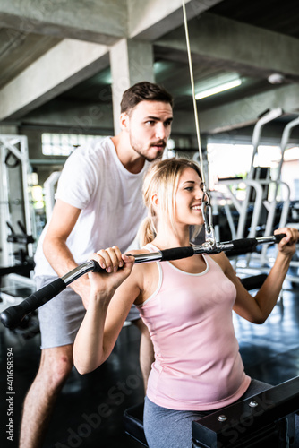 Cheerful young woman wearing pink sports bra while doing chin-up exercise with trainer man